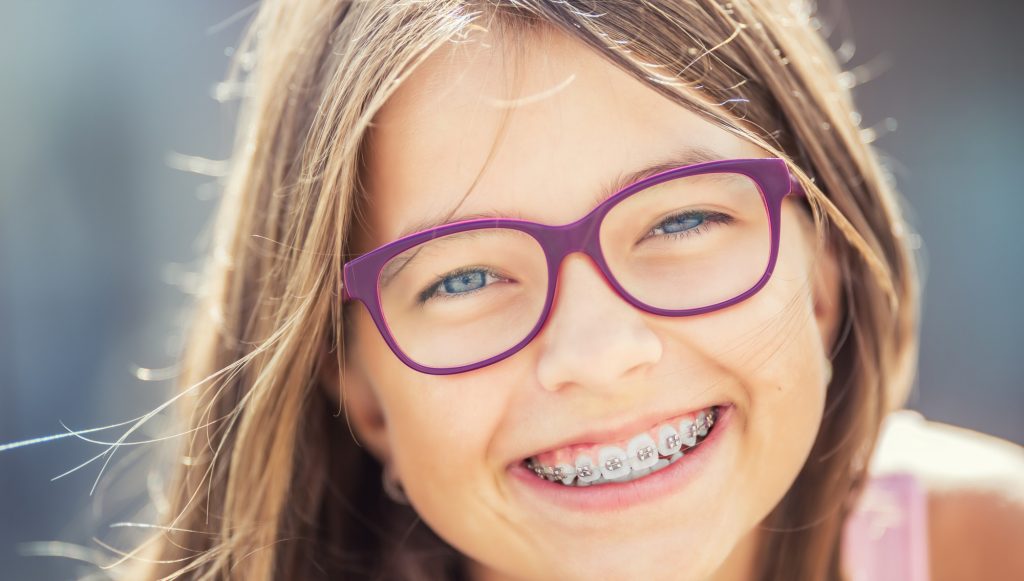 Happy smiling girl with dental braces and glasses. Young cute caucasian blond girl wearing teeth braces and glasses